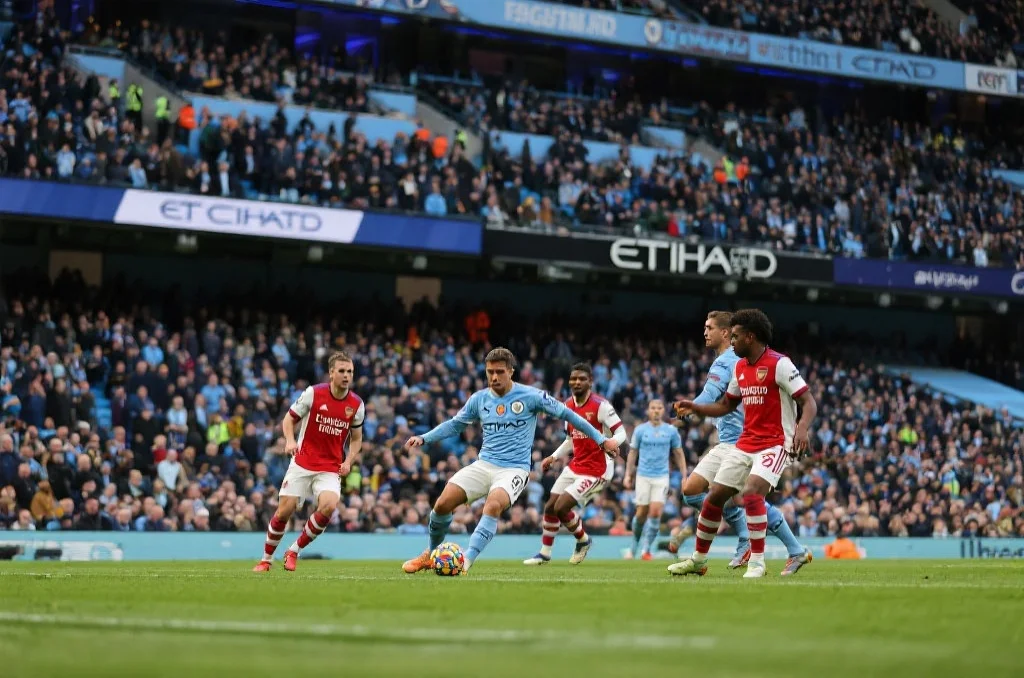 英超赛场上一场激烈的比赛，曼城、阿森纳和利物浦球员争夺足球，观众席座无虚席，现场气氛热烈